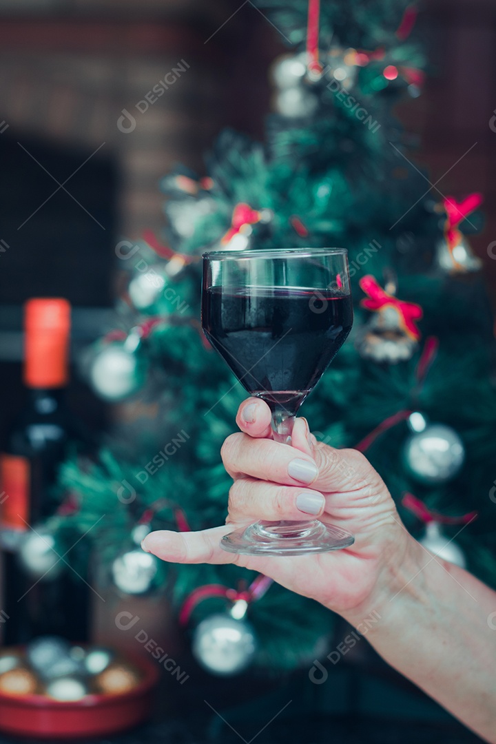 Segurando uma taça de vinho com árvore de Natal no fundo do quintal