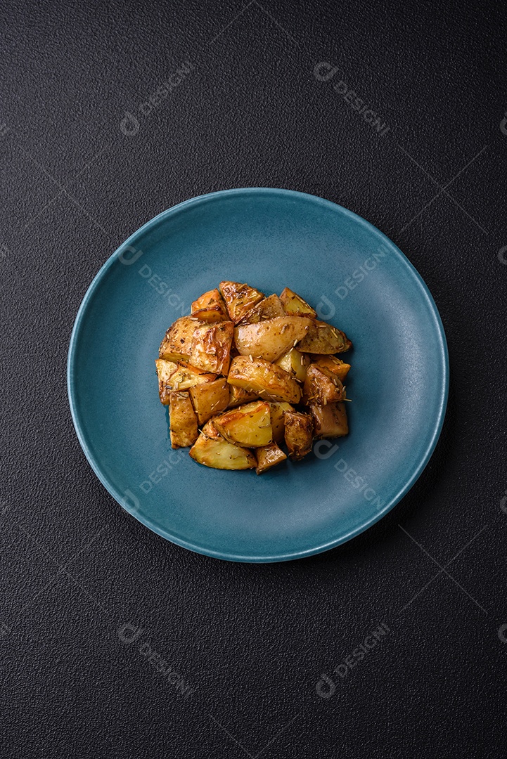 Deliciosas fatias de batata frita crocante com sal, especiarias e ervas sobre um fundo escuro de concreto