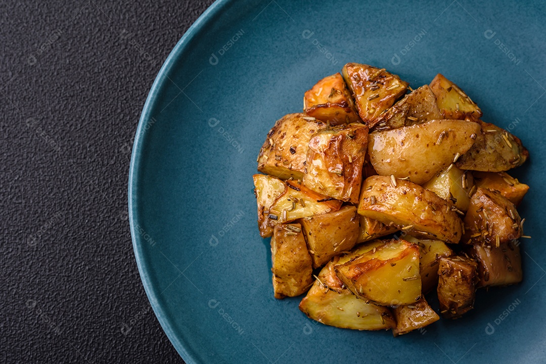 Deliciosas fatias de batata frita crocante com sal, especiarias e ervas sobre um fundo escuro de concreto