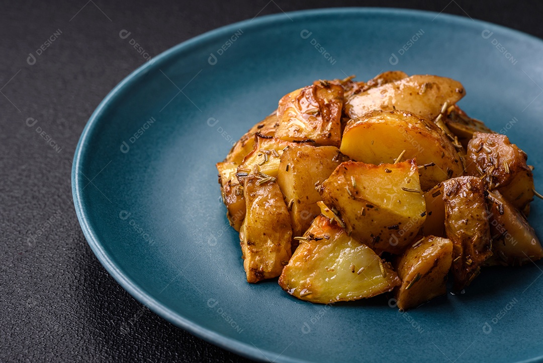 Deliciosas fatias de batata frita crocante com sal, especiarias e ervas sobre um fundo escuro de concreto