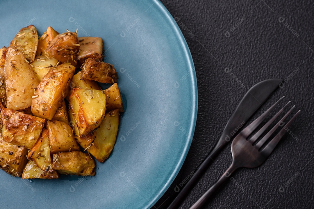 Deliciosas fatias de batata frita crocante com sal, especiarias e ervas sobre um fundo escuro de concreto