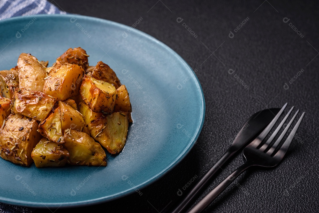 Deliciosas fatias de batata frita crocante com sal, especiarias e ervas sobre um fundo escuro de concreto