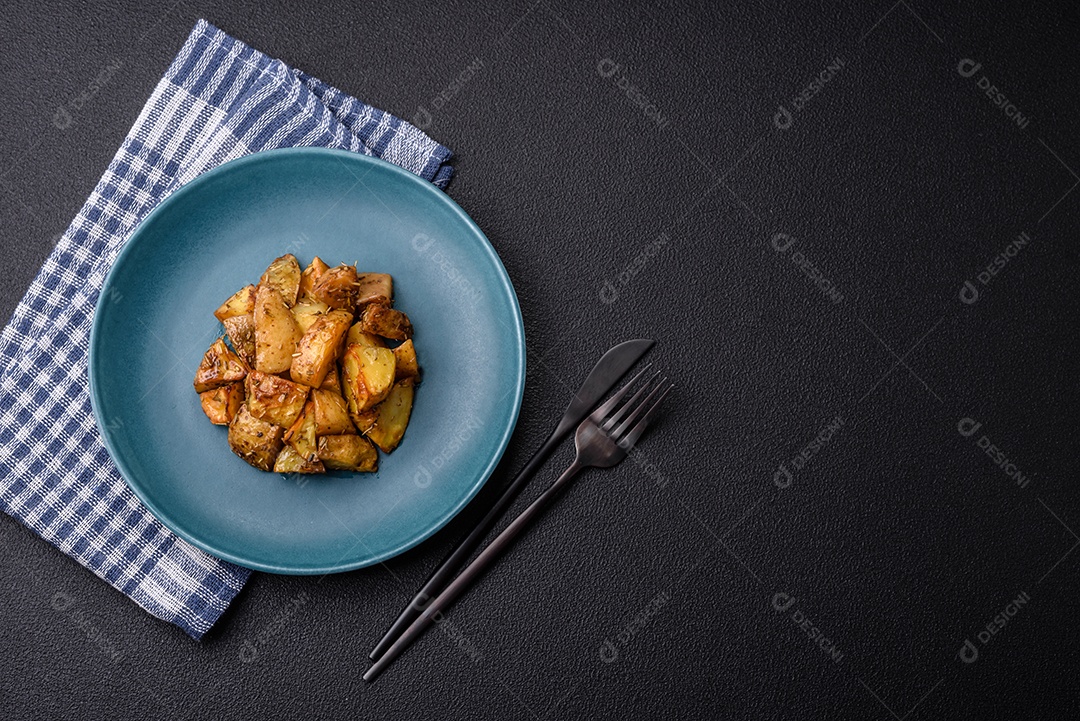 Deliciosas fatias de batata frita crocante com sal, especiarias e ervas sobre um fundo esc