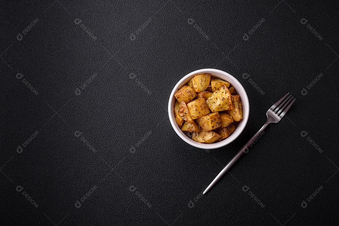 Deliciosas fatias de batata frita crocante com sal, especiarias e ervas sobre um fundo esc
