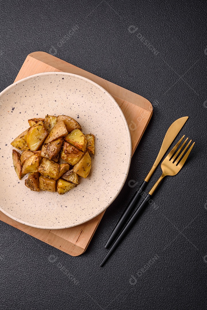 Deliciosas fatias de batata frita crocante com sal, especiarias e ervas sobre um fundo escuro de concreto