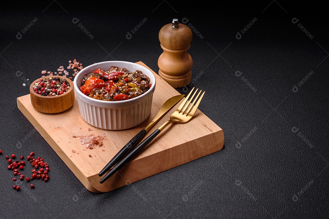 Salada quente com vitela, tomate, pimentão, abobrinha, gergelim, sal, especiarias e ervas sobre fundo escuro de concreto