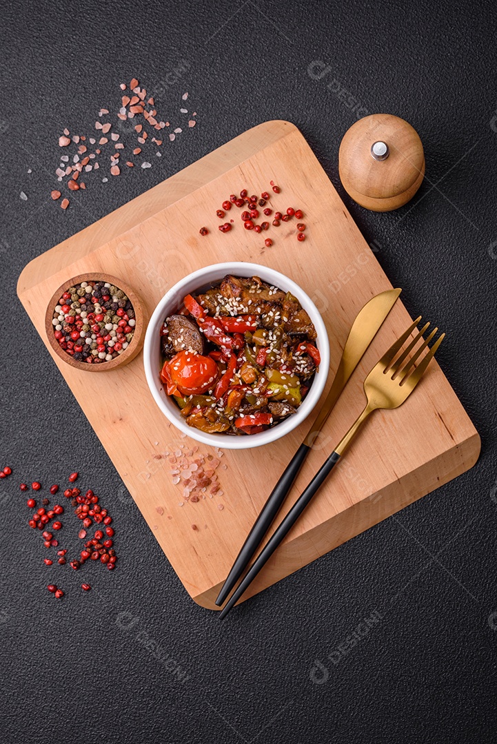 Salada quente com vitela, tomate, pimentão, abobrinha, gergelim, sal, especiarias e ervas sobre fundo escuro de concreto