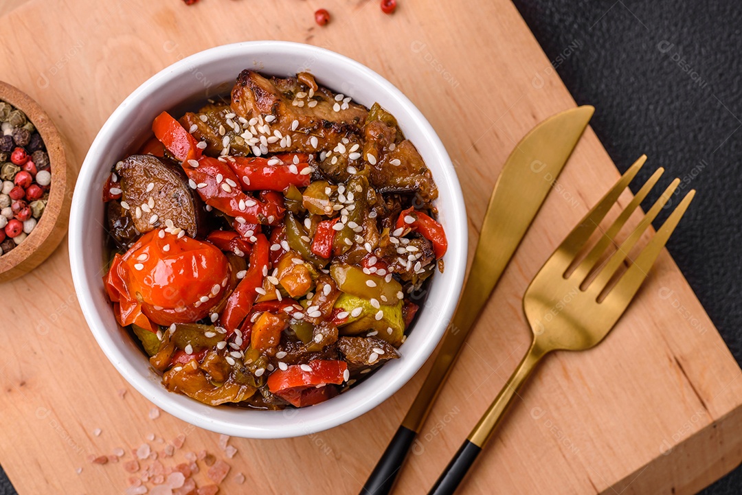 Salada quente com vitela, tomate, pimentão, abobrinha, gergelim, sal, especiarias e ervas sobre fundo escuro de concreto