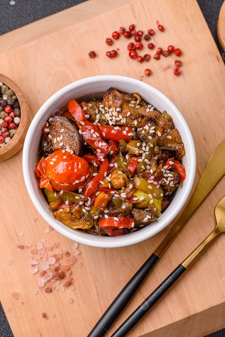 Salada quente com vitela, tomate, pimentão, abobrinha, gergelim, sal, especiarias e ervas sobre fundo escuro de concreto