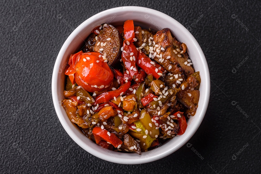 Salada quente com vitela, tomate, pimentão, abobrinha, gergelim, sal, especiarias e ervas sobre fundo escuro de concreto