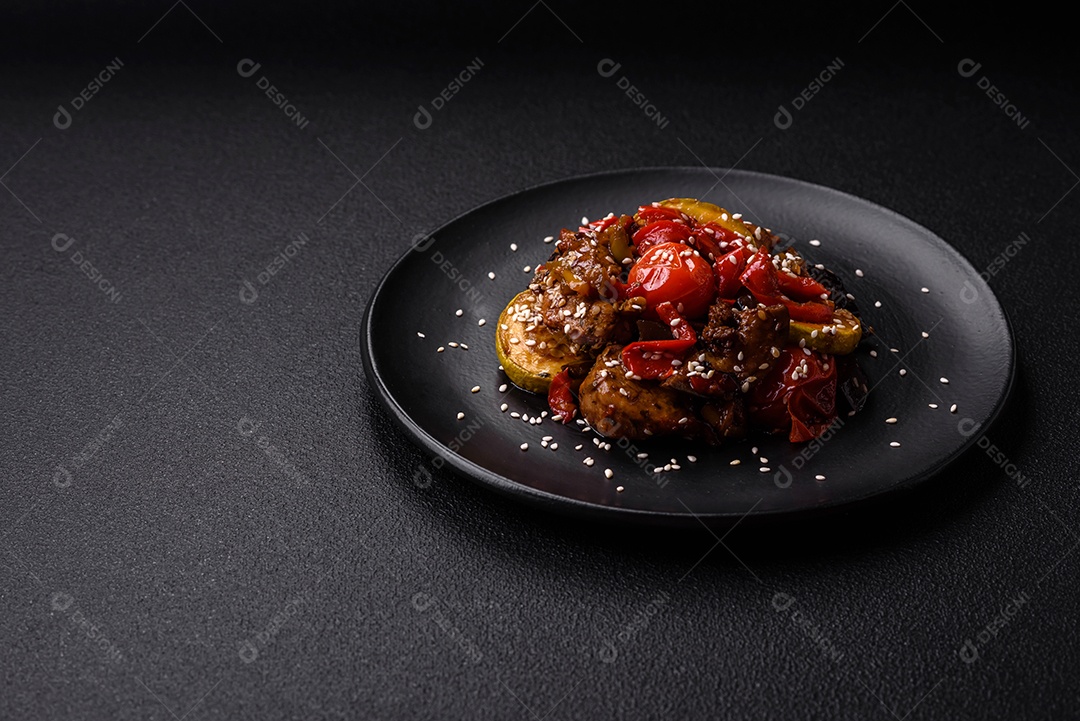 Salada quente com vitela, tomate, pimentão, abobrinha, gergelim, sal, especiarias e ervas sobre fundo escuro de concreto