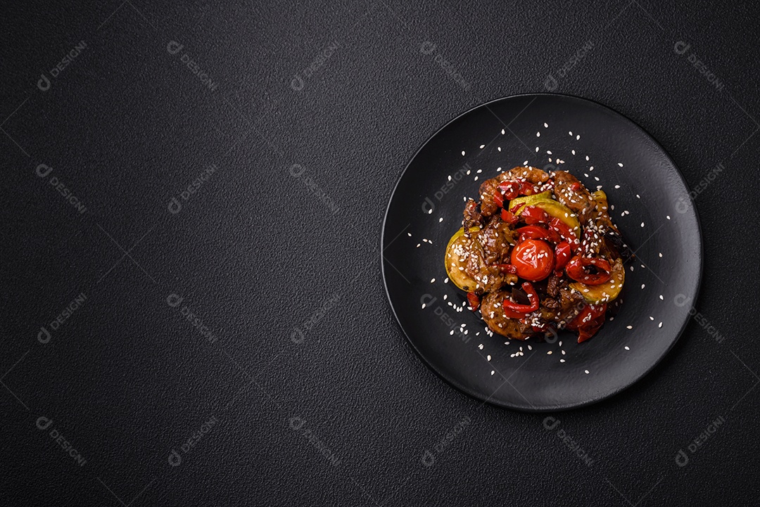Salada quente com vitela, tomate, pimentão, abobrinha, gergelim, sal, especiarias e ervas sobre fundo escuro de concreto