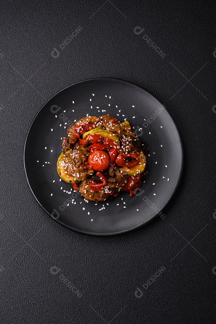 Salada quente com vitela, tomate, pimentão, abobrinha, gergelim, sal, especiarias e ervas sobre fundo escuro de concreto