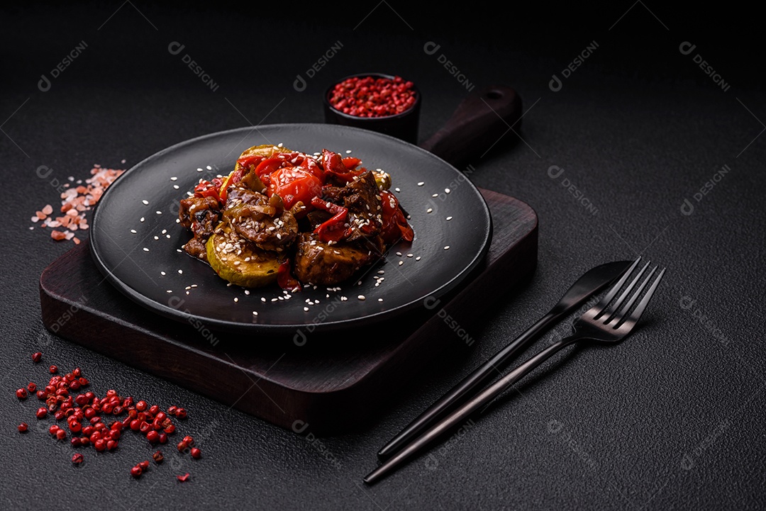 Salada quente com vitela, tomate, pimentão, abobrinha, gergelim, sal, especiarias e ervas sobre fundo escuro de concreto