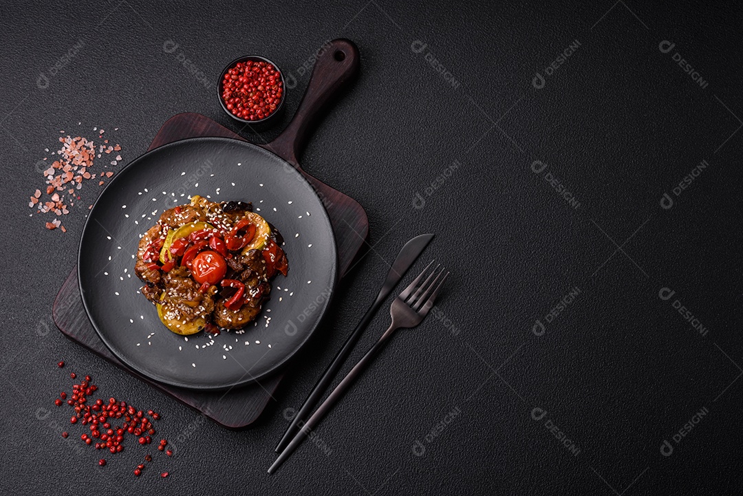 Salada quente com vitela, tomate, pimentão, abobrinha, gergelim, sal, especiarias e ervas sobre fundo escuro de concreto