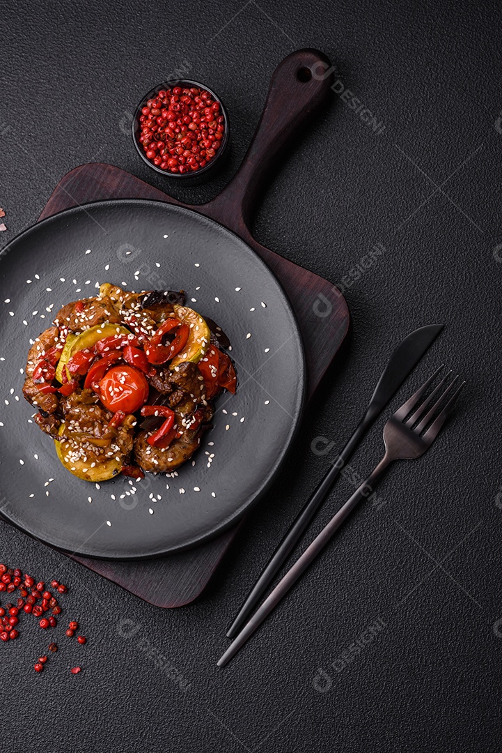 Salada quente com vitela, tomate, pimentão, abobrinha, gergelim, sal, especiarias e ervas sobre fundo escuro de concreto