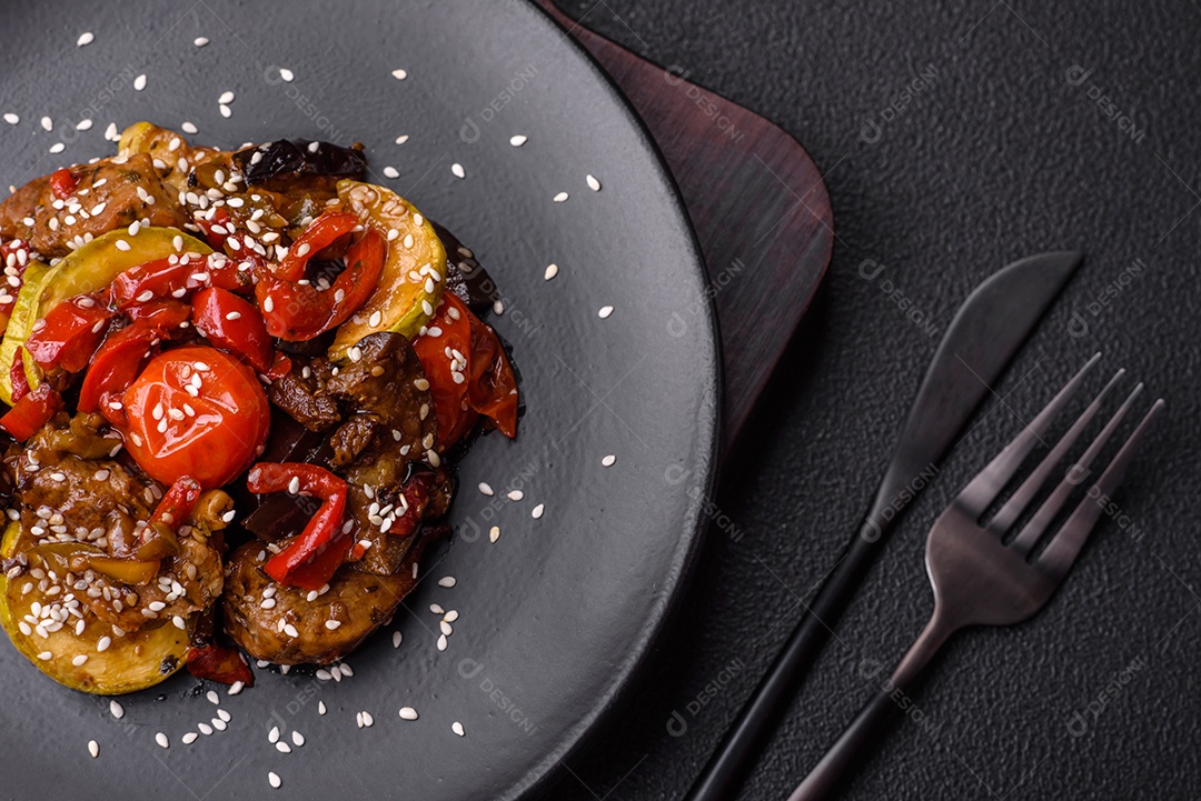 Salada quente com vitela, tomate, pimentão, abobrinha, gergelim, sal, especiarias e ervas sobre fundo escuro de concreto