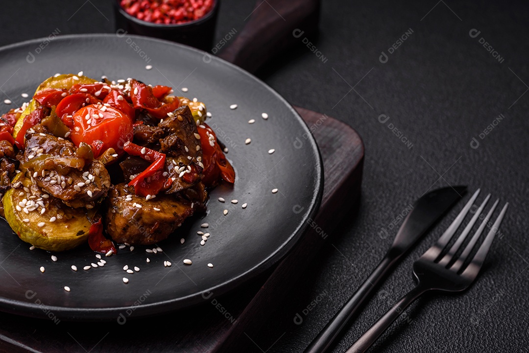 Salada quente com vitela, tomate, pimentão, abobrinha, gergelim, sal, especiarias e ervas sobre fundo escuro de concreto