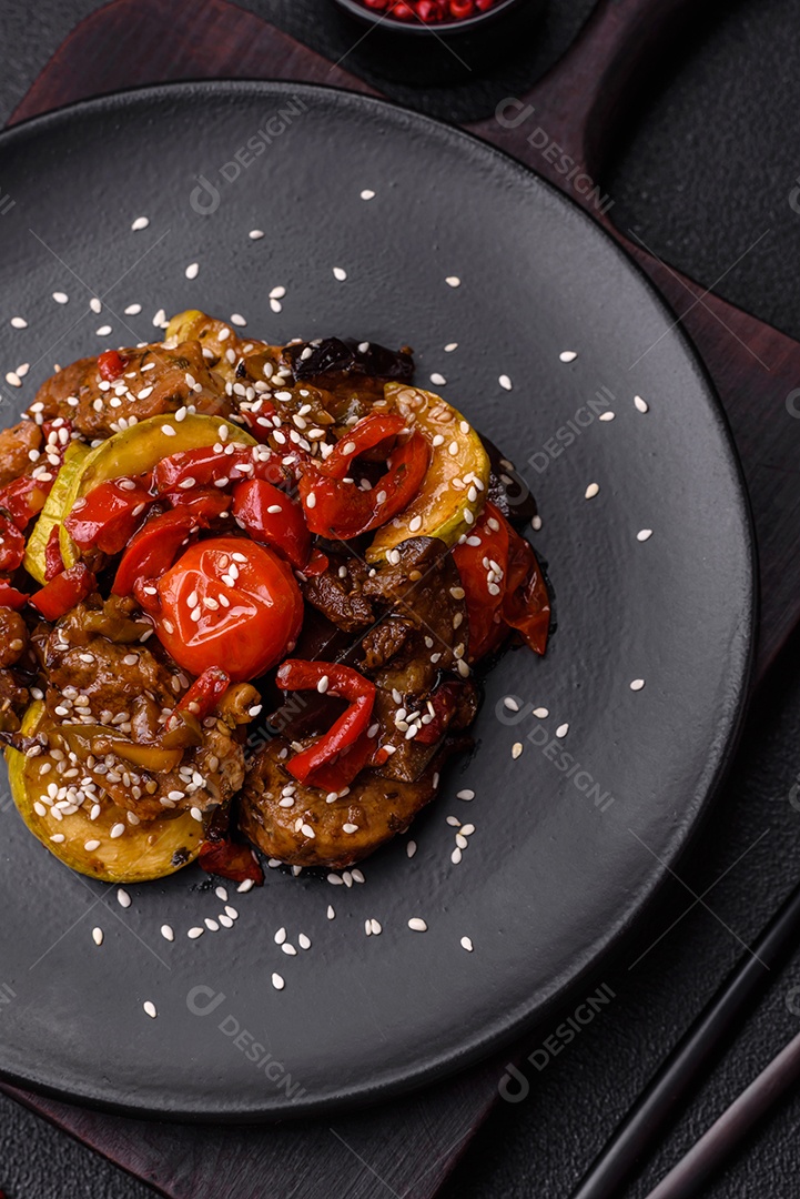Salada quente com vitela, tomate, pimentão, abobrinha, gergelim, sal, especiarias e ervas sobre fundo escuro de concreto