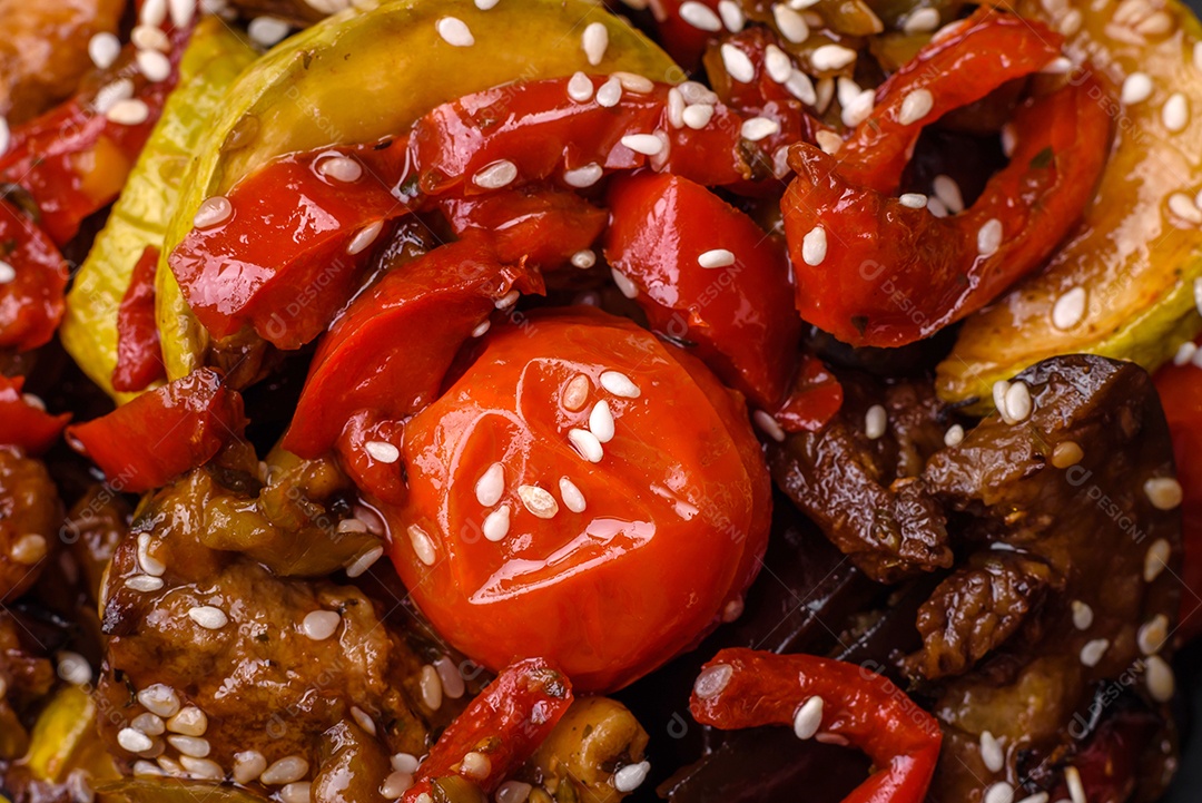 Salada quente com vitela, tomate, pimentão, abobrinha, gergelim, sal, especiarias e ervas sobre fundo escuro de concreto