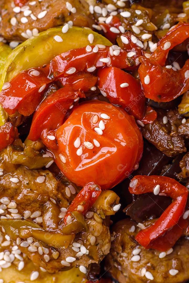 Salada quente com vitela, tomate, pimentão, abobrinha, gergelim, sal, especiarias e ervas sobre fundo escuro de concreto