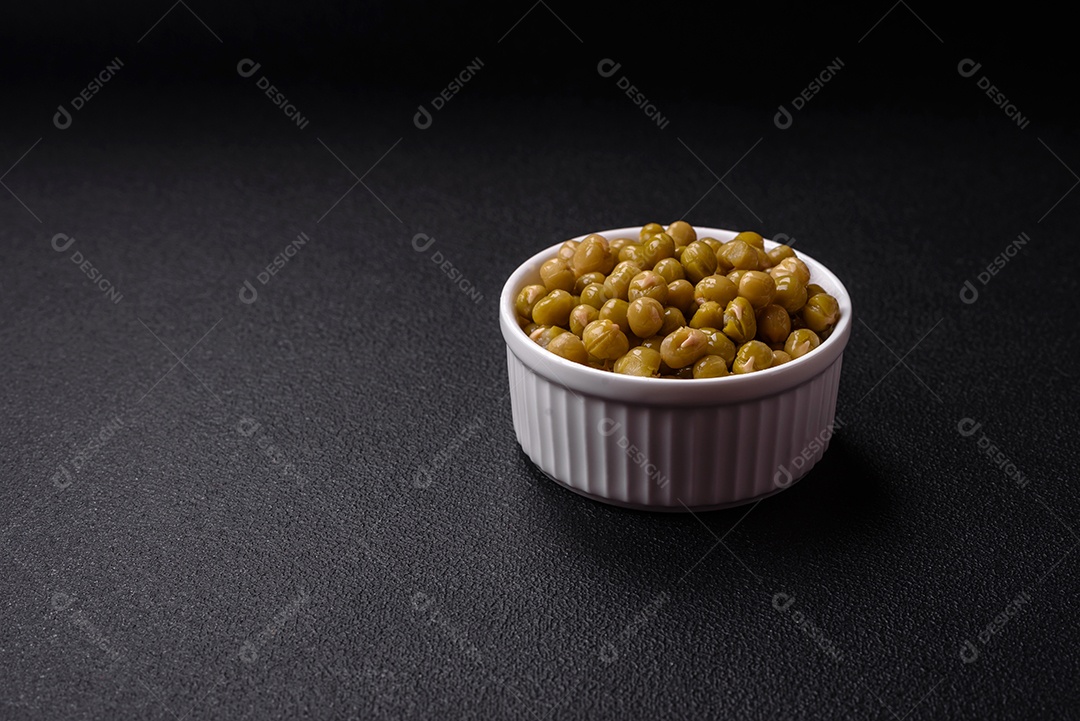 Deliciosas ervilhas enlatadas com sal e especiarias em uma tigela branca sobre um fundo escuro de concreto