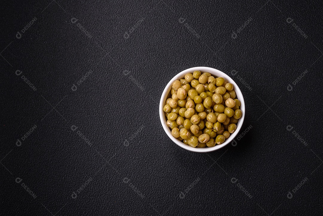 Deliciosas ervilhas enlatadas com sal e especiarias em uma tigela branca sobre um fundo escuro de concreto