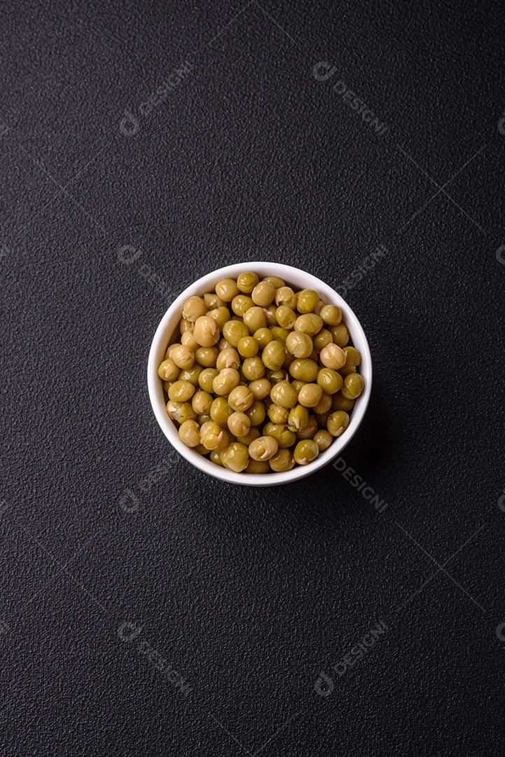 Deliciosas ervilhas enlatadas com sal e especiarias em uma tigela branca sobre um fundo escuro de concreto