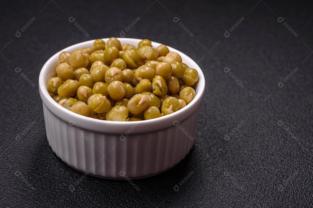 Deliciosas ervilhas enlatadas com sal e especiarias em uma tigela branca sobre um fundo escuro de concreto
