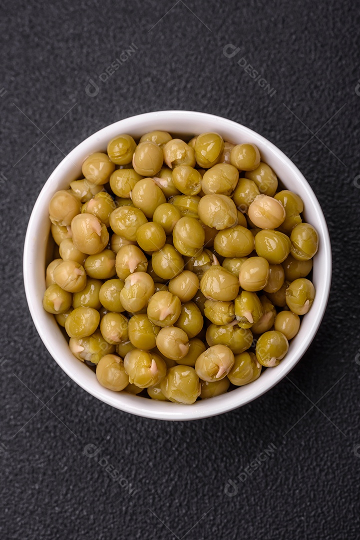 Deliciosas ervilhas enlatadas com sal e especiarias em uma tigela branca sobre um fundo escuro de concreto