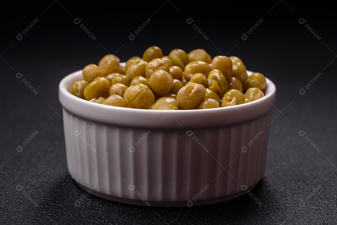 Deliciosas ervilhas enlatadas com sal e especiarias em uma tigela branca sobre um fundo escuro de concreto