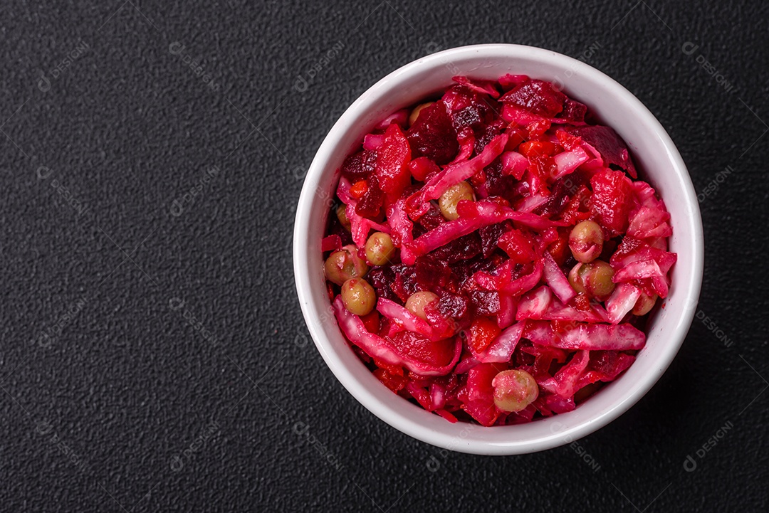 Deliciosa salada vinigret suculenta de legumes cozidos, batatas, beterraba, maconha, repolho e cenoura com sal e especiarias em um fundo escuro de concreto