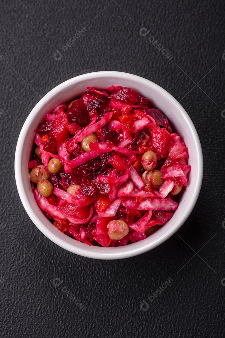 Deliciosa salada vinigret suculenta de legumes cozidos, batatas, beterraba, maconha, repolho e cenoura com sal e especiarias em um fundo escuro de concreto