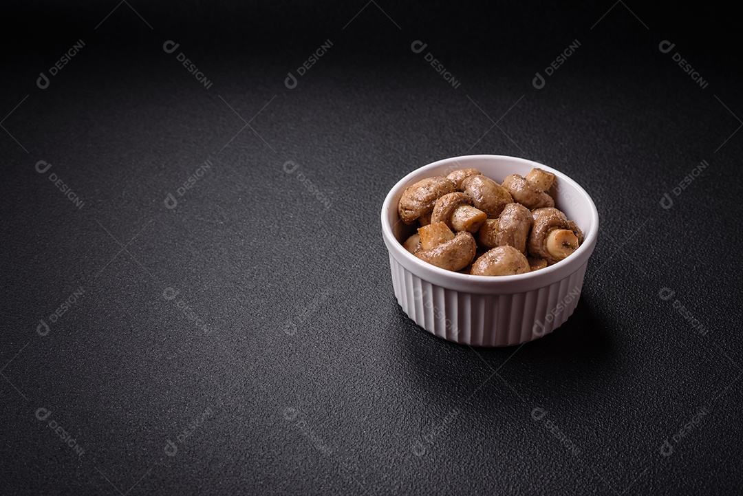 Deliciosos champignon inteiros e suculentos assados ​​na grelha com sal e especiarias em uma placa de cerâmica sobre um fundo escuro de concreto