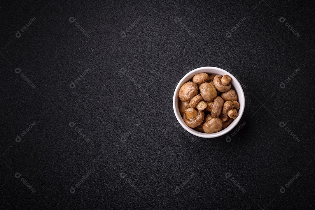 Deliciosos champignon inteiros e suculentos assados ​​na grelha com sal e especiarias em uma placa de cerâmica sobre um fundo escuro de concreto