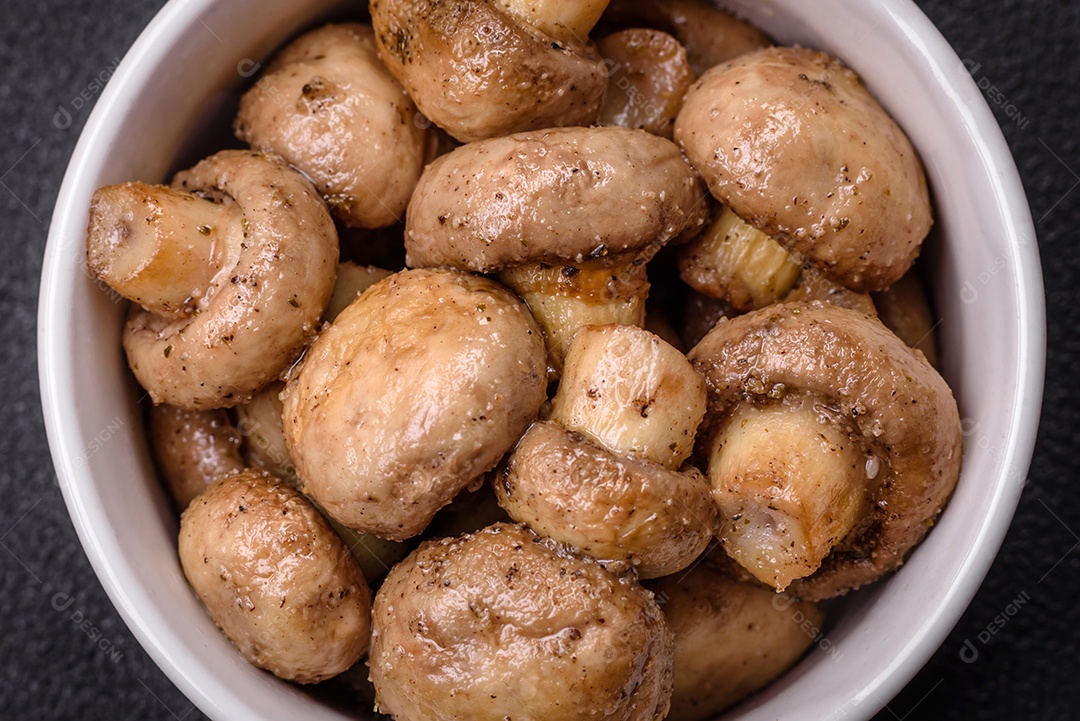 Deliciosos champignon inteiros e suculentos assados ​​na grelha com sal e especiarias em uma placa de cerâmica sobre um fundo escuro de concreto