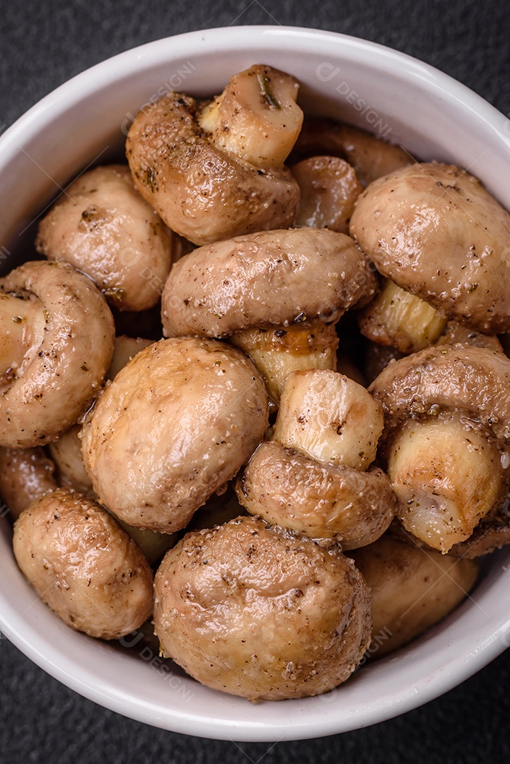 Deliciosos champignon inteiros e suculentos assados ​​na grelha com sal e especiarias em uma placa de cerâmica sobre um fundo escuro de concreto