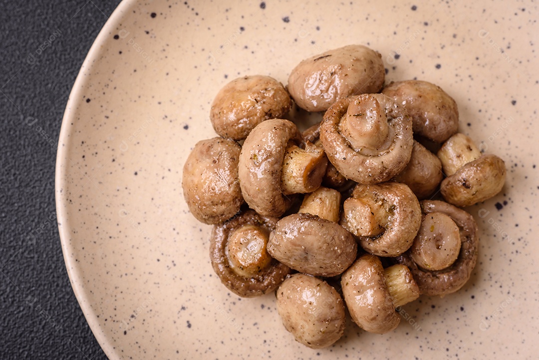 Deliciosos champignon inteiros e suculentos assados ​​na grelha com sal e especiarias em uma placa de cerâmica sobre um fundo escuro de concreto