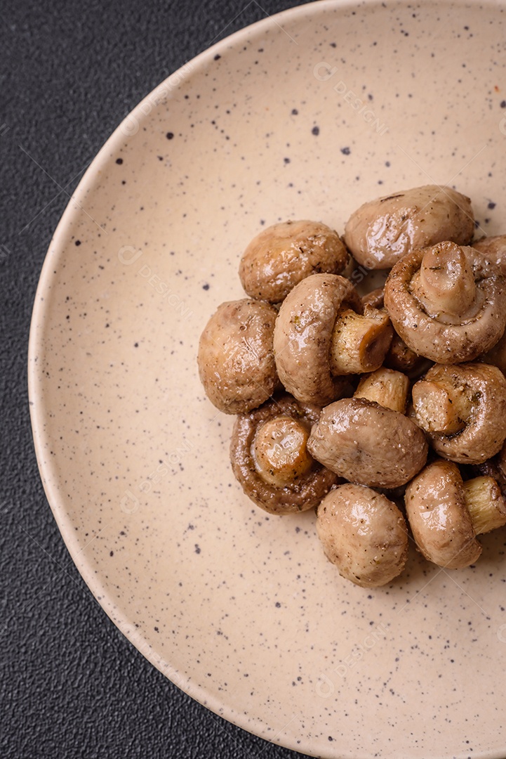 Deliciosos champignon inteiros e suculentos assados ​​na grelha com sal e especiarias em uma placa de cerâmica sobre um fundo escuro de concreto