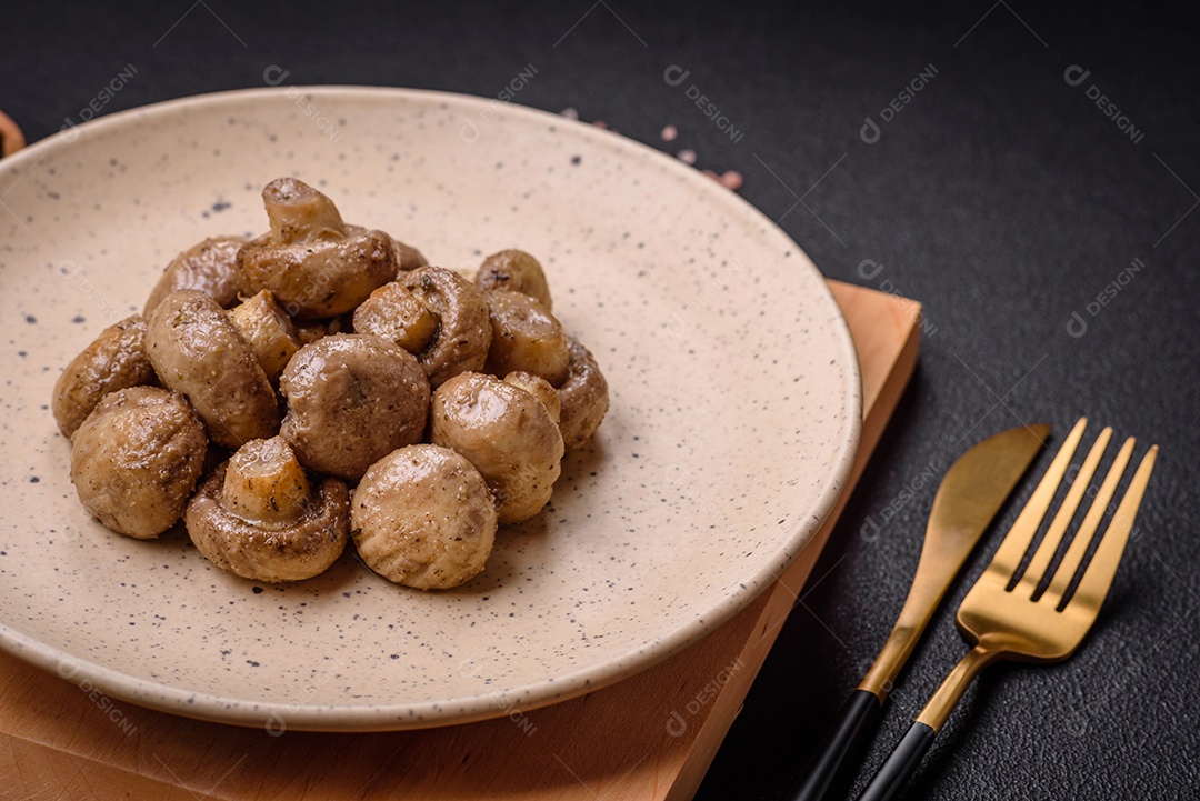 Deliciosos champignon inteiros e suculentos assados ​​na grelha com sal e especiarias em uma placa de cerâmica sobre um fundo escuro de concreto