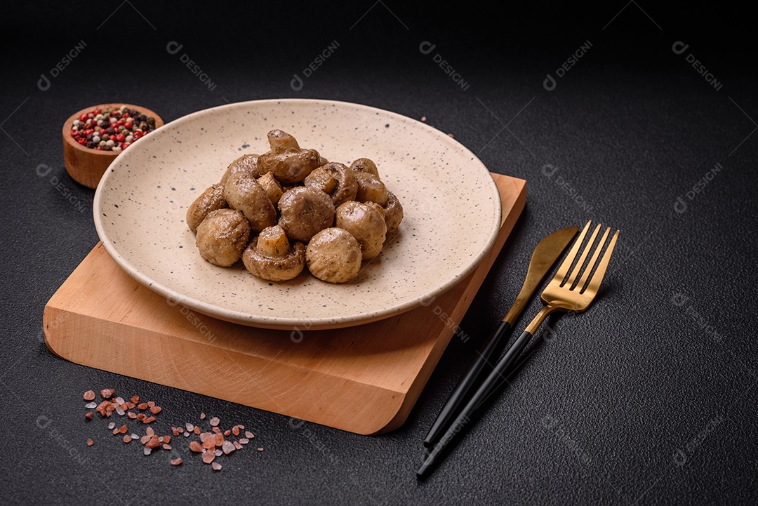 Deliciosos champignon inteiros e suculentos assados ​​na grelha com sal e especiarias em uma placa de cerâmica sobre um fundo escuro de concreto