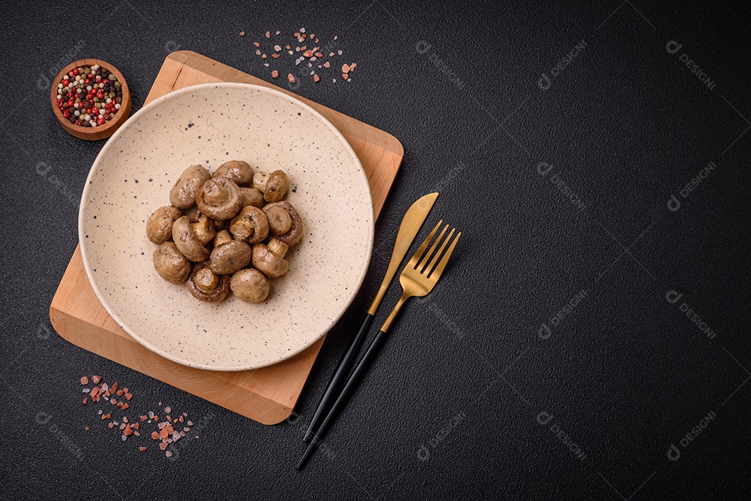 Deliciosos champignon inteiros e suculentos assados ​​na grelha com sal e especiarias em uma placa de cerâmica sobre um fundo escuro de concreto