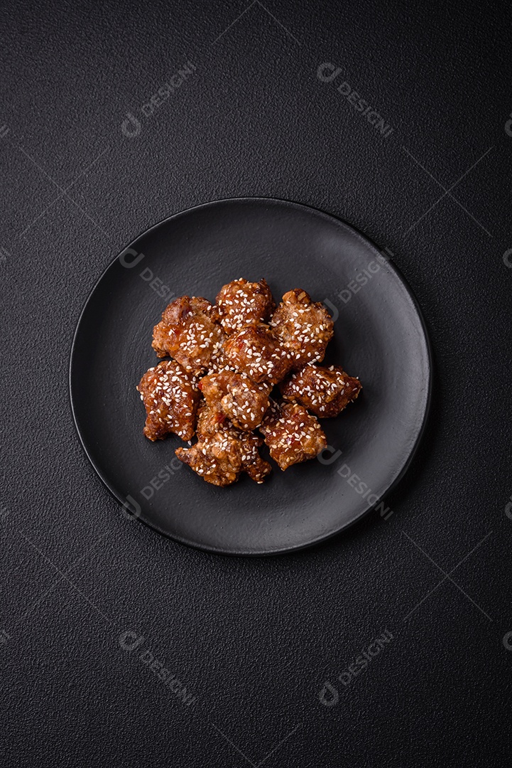 Delicioso prato asiático com pedaços de frango em molho teriyaki com sal e especiarias sobre fundo escuro de concreto