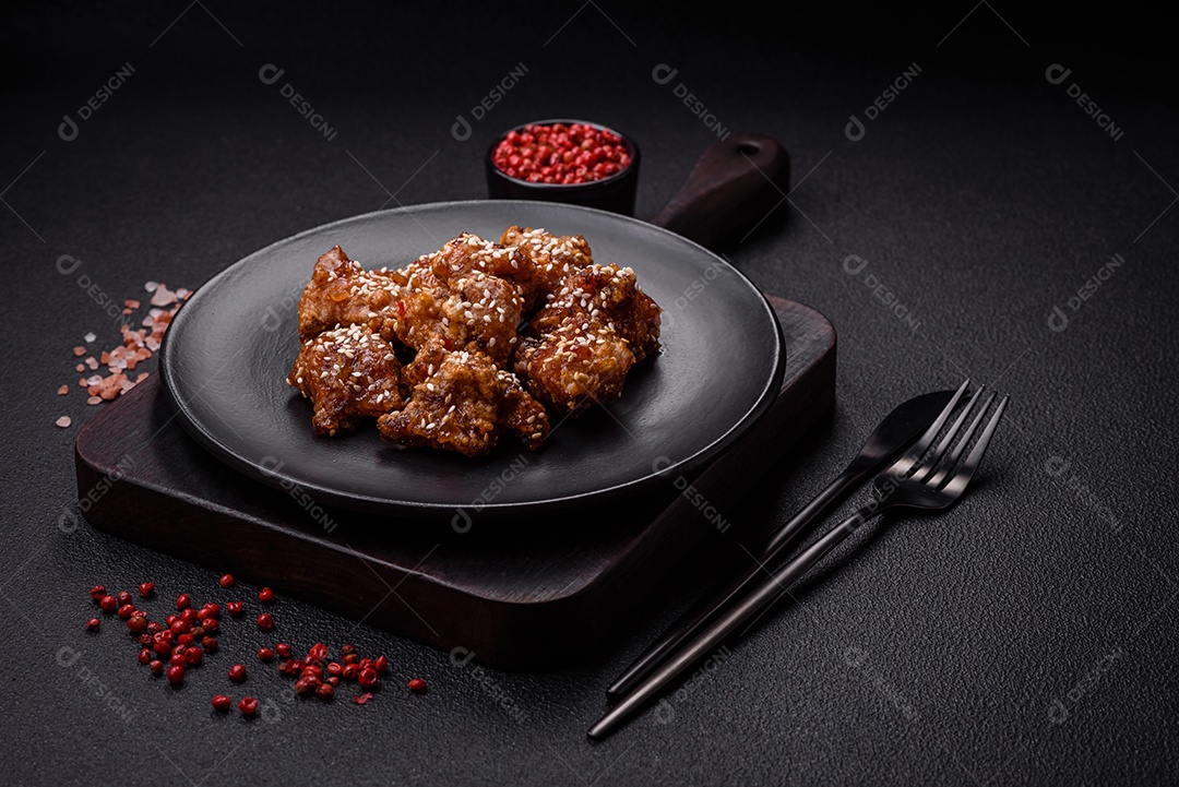 Delicioso prato asiático com pedaços de frango em molho teriyaki com sal e especiarias sobre fundo escuro de concreto