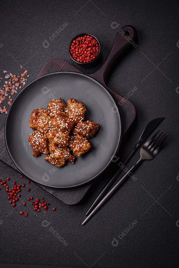 Delicioso prato asiático com pedaços de frango em molho teriyaki com sal e especiarias sobre fundo escuro de concreto