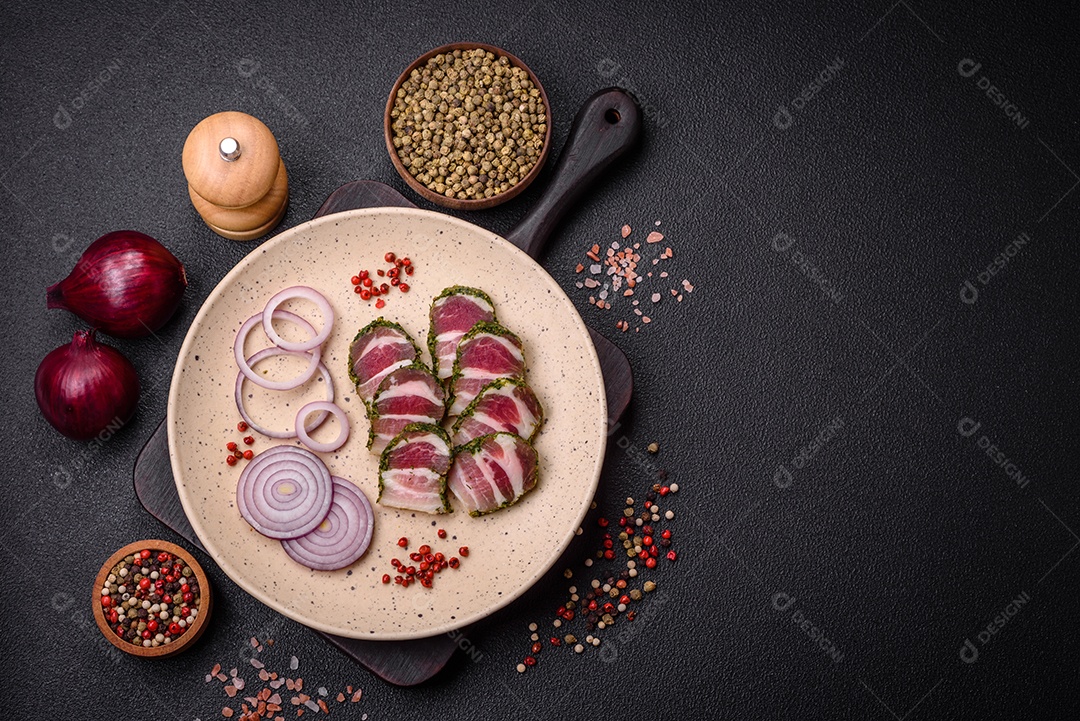 Deliciosas listras de bacon fresco com especiarias e sal sobre um fundo escuro de concreto