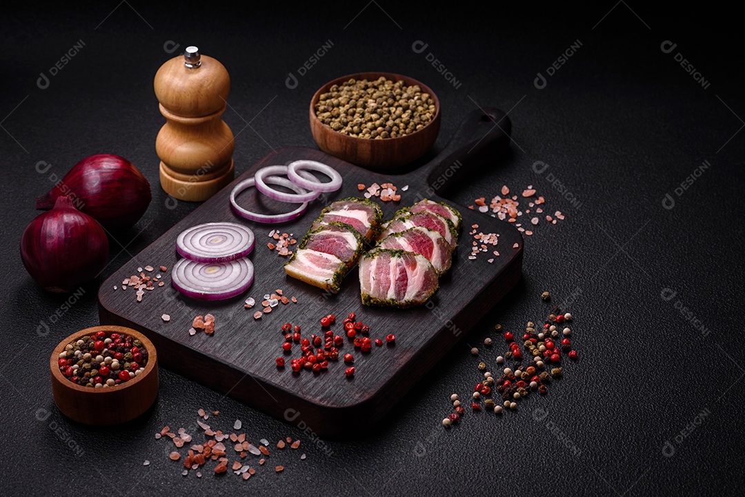 Deliciosas listras de bacon fresco com especiarias e sal sobre um fundo escuro de concreto