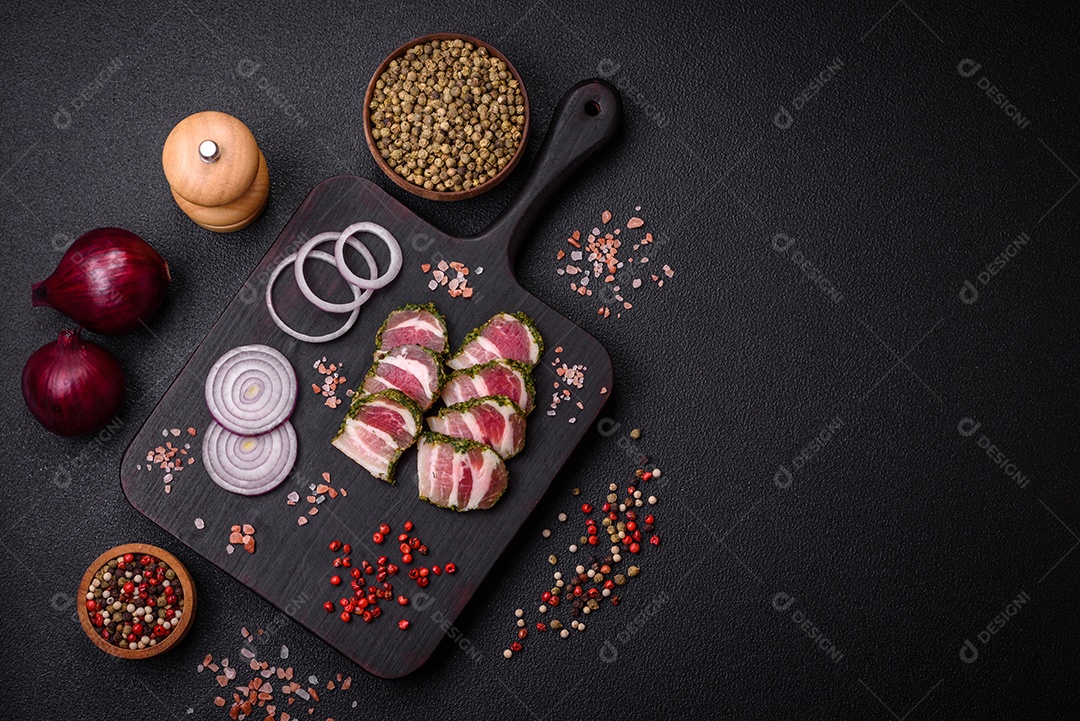 Deliciosas listras de bacon fresco com especiarias e sal sobre um fundo escuro de concreto