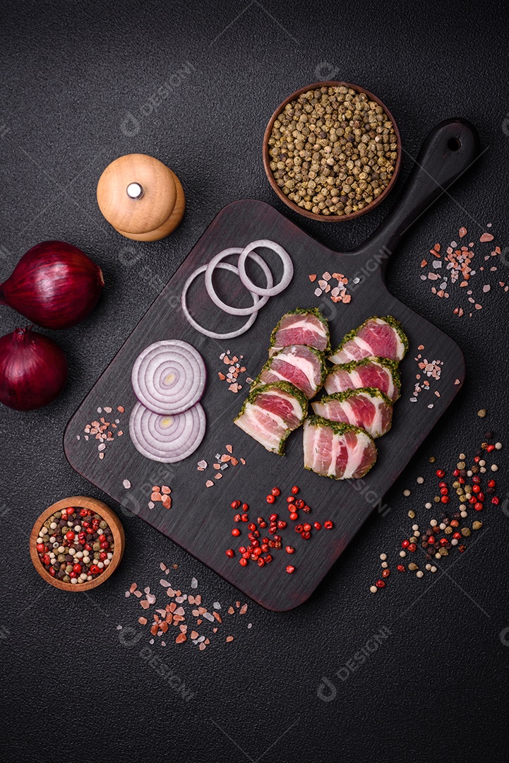 Deliciosas listras de bacon fresco com especiarias e sal sobre um fundo escuro de concreto