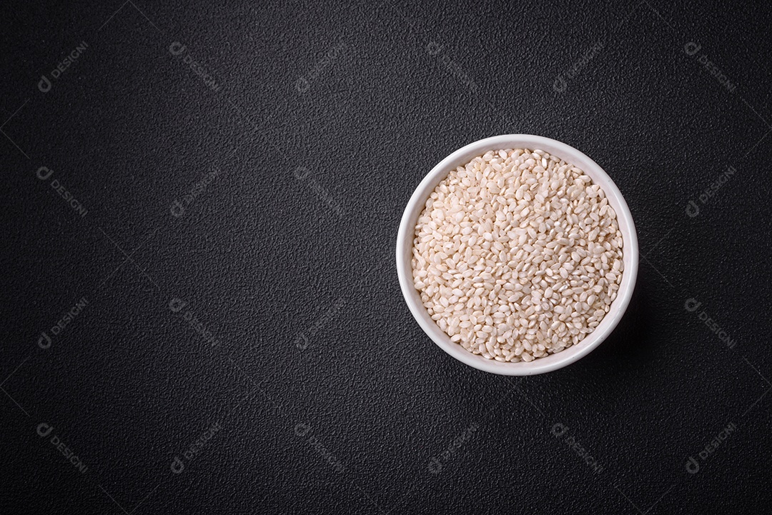 Arroz branco cru em uma tigela redonda de cerâmica sobre um fundo escuro de concreto. Cozinhar comida asiática